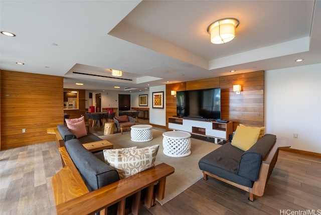 living room featuring a raised ceiling, wooden walls, and hardwood / wood-style floors