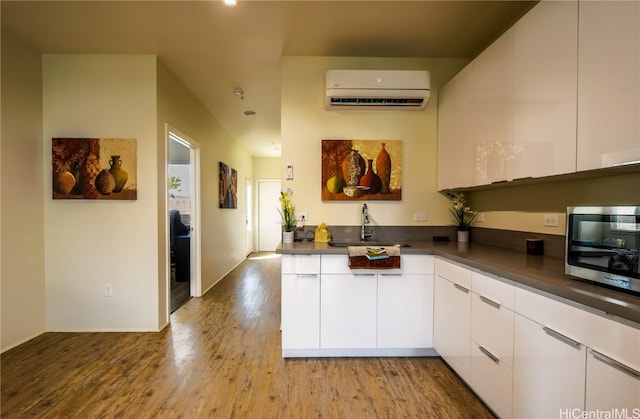 kitchen featuring sink, light hardwood / wood-style flooring, a wall mounted air conditioner, and white cabinets