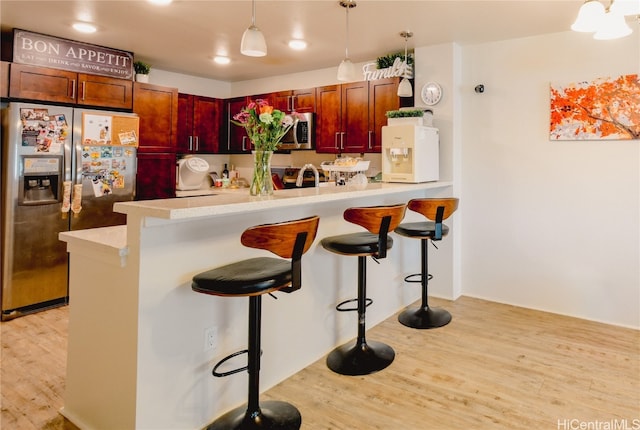 kitchen featuring kitchen peninsula, hanging light fixtures, a breakfast bar area, light hardwood / wood-style floors, and stainless steel appliances