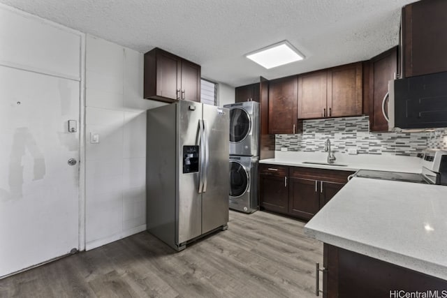 kitchen featuring backsplash, appliances with stainless steel finishes, light wood-type flooring, sink, and stacked washer and clothes dryer