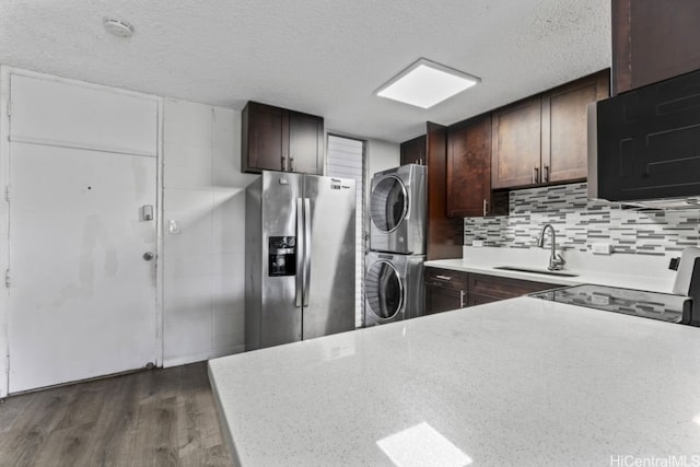 kitchen with sink, backsplash, stainless steel fridge, stacked washer / drying machine, and dark hardwood / wood-style floors