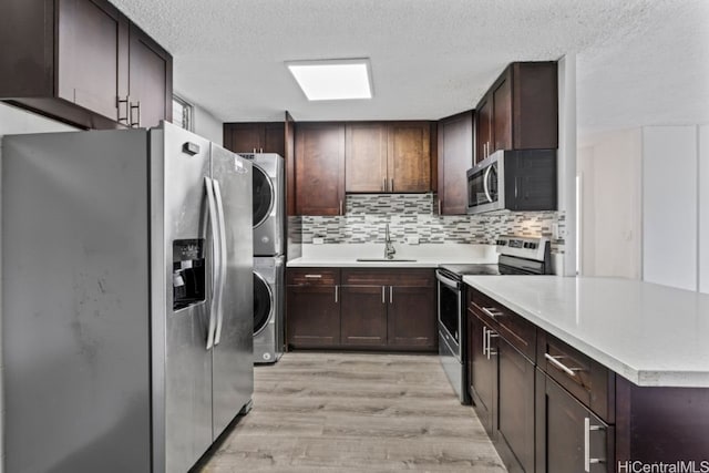 kitchen featuring stacked washer and dryer, stainless steel appliances, backsplash, sink, and light hardwood / wood-style floors