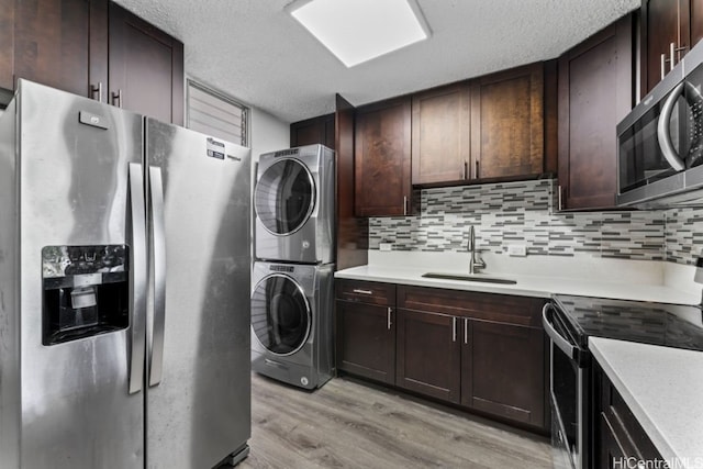 clothes washing area with sink, a textured ceiling, stacked washer / drying machine, and light hardwood / wood-style floors