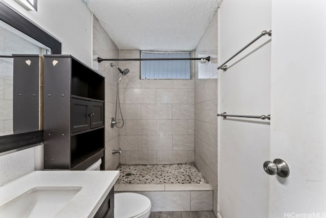 bathroom with tiled shower, hardwood / wood-style flooring, toilet, vanity, and a textured ceiling