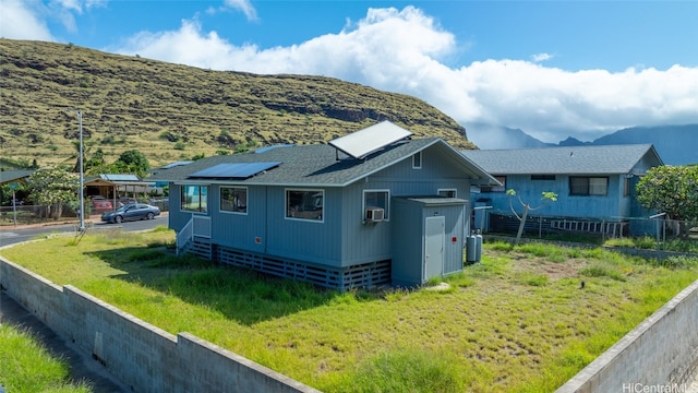 view of side of home with cooling unit, solar panels, a mountain view, and a lawn