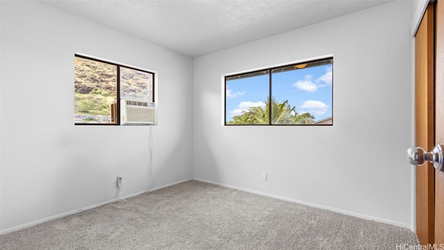 carpeted empty room featuring a healthy amount of sunlight, a textured ceiling, and cooling unit