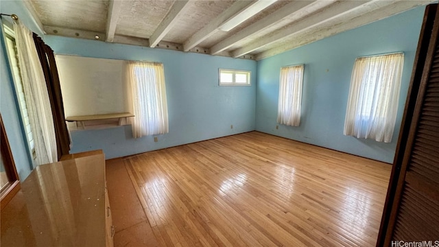 unfurnished bedroom with lofted ceiling with beams and light hardwood / wood-style flooring