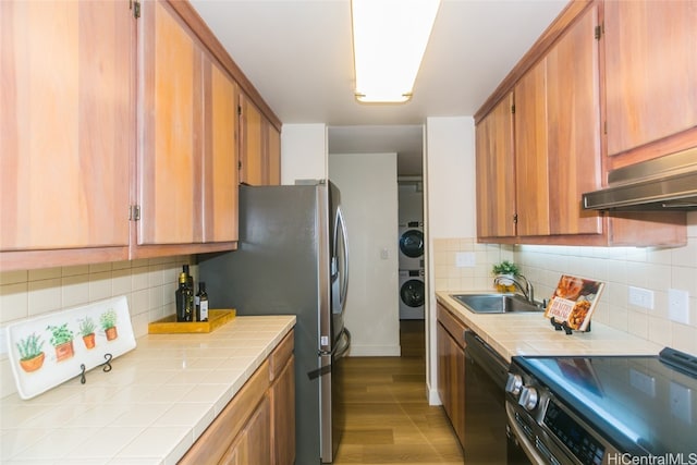 kitchen with appliances with stainless steel finishes, light wood-type flooring, tile countertops, backsplash, and stacked washer and clothes dryer