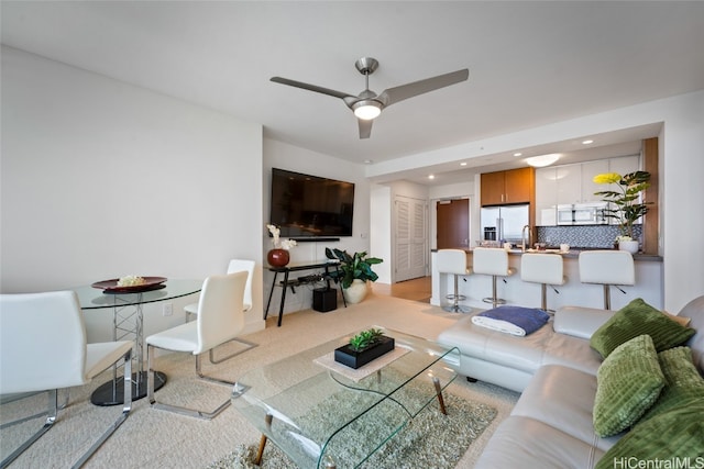 living room with ceiling fan, light carpet, and sink