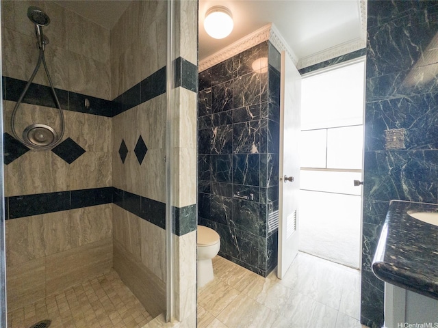 bathroom featuring vanity, marble finish floor, toilet, tile walls, and a tile shower