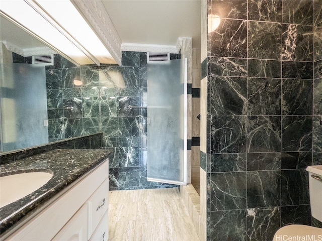 bathroom with a tile shower, tile walls, toilet, vanity, and crown molding