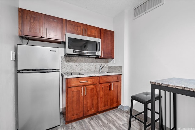 kitchen with a textured ceiling, visible vents, a sink, light wood finished floors, and stainless steel appliances