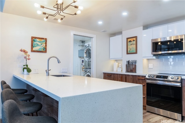 kitchen featuring light hardwood / wood-style flooring, sink, white cabinetry, appliances with stainless steel finishes, and stacked washer / drying machine