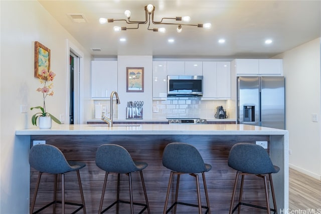 kitchen featuring stainless steel appliances, white cabinetry, sink, a breakfast bar, and wood-type flooring