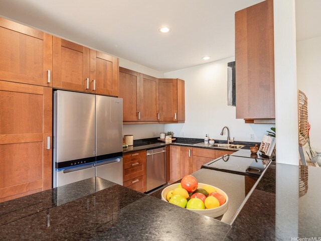kitchen featuring dark stone countertops, brown cabinets, a sink, appliances with stainless steel finishes, and recessed lighting
