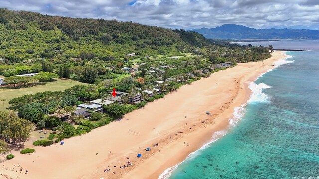 aerial view with a water and mountain view, a wooded view, and a view of the beach