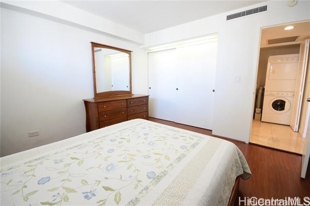 bedroom featuring a closet, stacked washer / dryer, and dark wood-type flooring