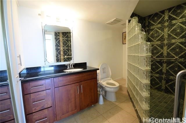 bathroom featuring vanity, a tile shower, toilet, and tile patterned flooring