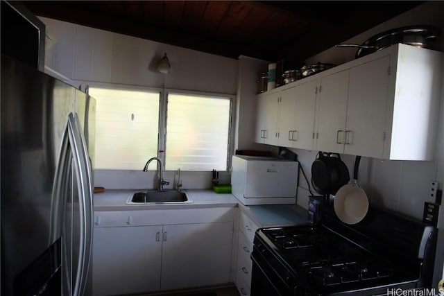 kitchen featuring black gas range, white cabinetry, sink, and stainless steel refrigerator