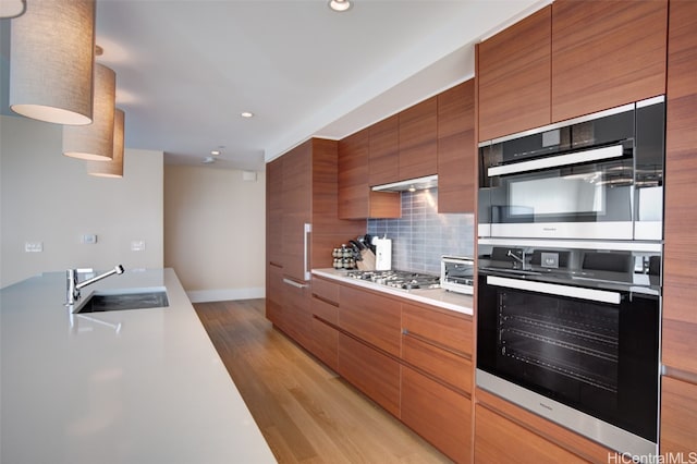 kitchen with appliances with stainless steel finishes, sink, light wood-type flooring, and decorative backsplash