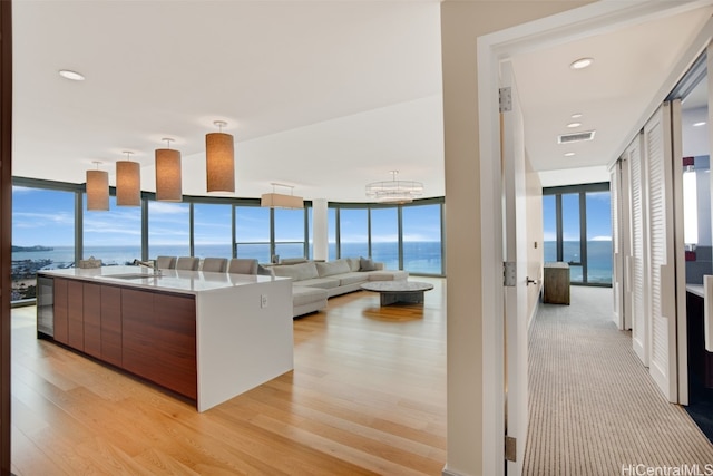 kitchen with floor to ceiling windows, a water view, light hardwood / wood-style flooring, an inviting chandelier, and a kitchen island with sink