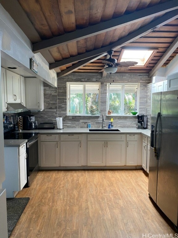 kitchen with backsplash, sink, vaulted ceiling with skylight, stainless steel appliances, and light hardwood / wood-style floors