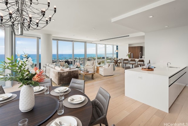 dining space featuring an inviting chandelier, expansive windows, light hardwood / wood-style floors, sink, and a water view