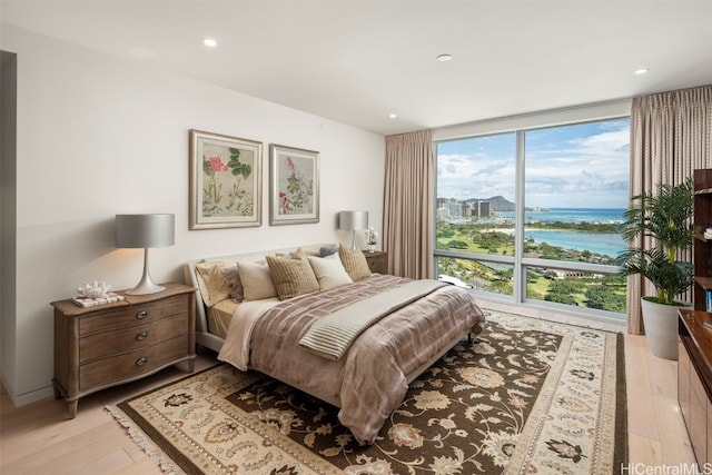 bedroom with expansive windows, a water view, and light hardwood / wood-style floors