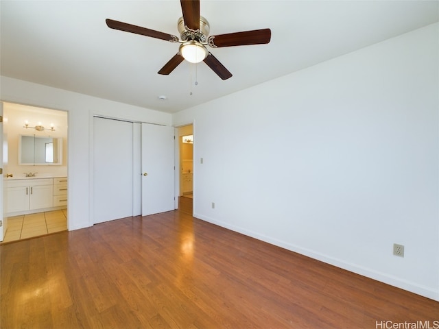 unfurnished bedroom featuring ceiling fan, connected bathroom, wood-type flooring, a closet, and sink