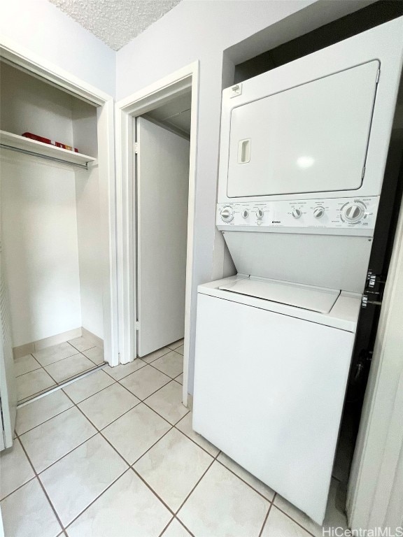 laundry room with light tile patterned floors, a textured ceiling, and stacked washer and dryer