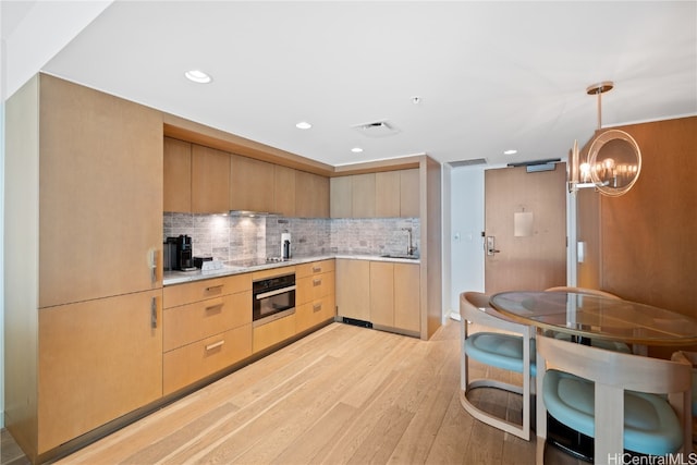 kitchen with stainless steel oven, light brown cabinetry, decorative backsplash, sink, and light hardwood / wood-style flooring