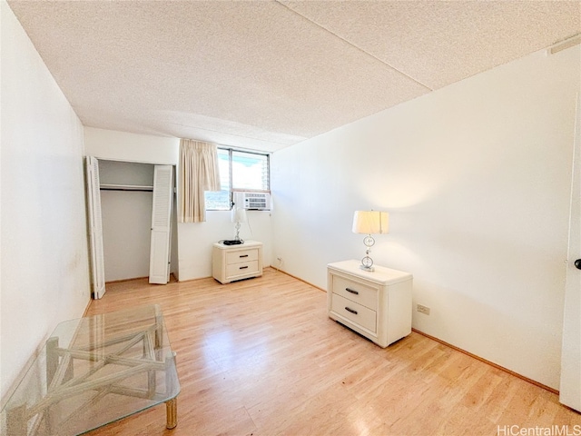 unfurnished bedroom featuring a textured ceiling, light wood-type flooring, cooling unit, and a closet