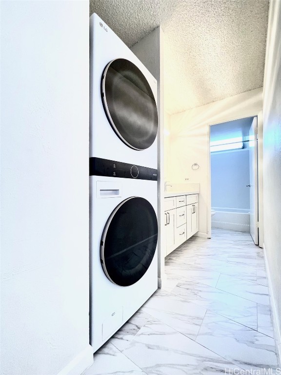 laundry room featuring a textured ceiling and stacked washer / drying machine