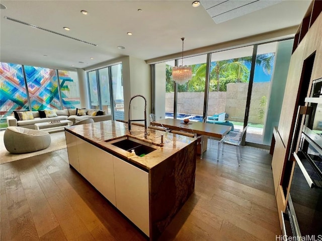 kitchen featuring decorative light fixtures, white cabinetry, light hardwood / wood-style floors, and an island with sink