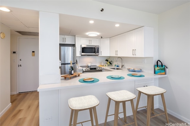 kitchen featuring white cabinets, appliances with stainless steel finishes, a breakfast bar, light hardwood / wood-style floors, and sink