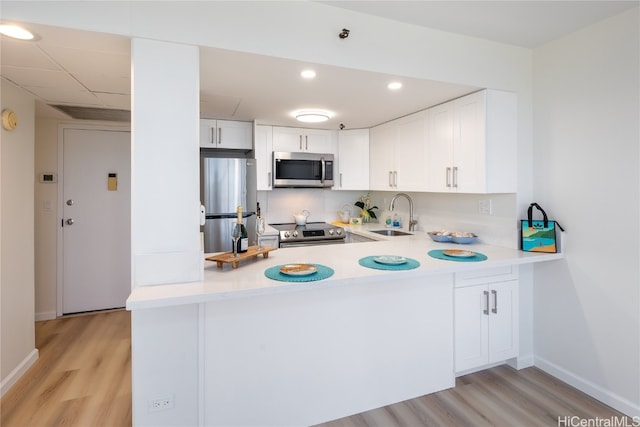 kitchen with kitchen peninsula, white cabinets, sink, light hardwood / wood-style floors, and stainless steel appliances