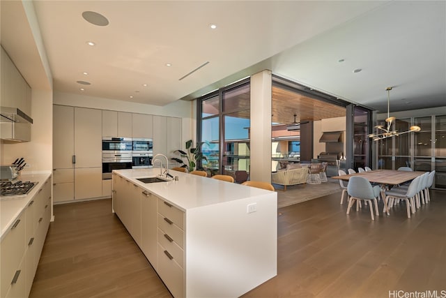 kitchen with a center island with sink, range hood, pendant lighting, light hardwood / wood-style floors, and sink