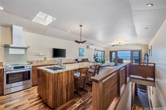 kitchen featuring sink, light wood-type flooring, lofted ceiling, stainless steel stove, and a kitchen island with sink