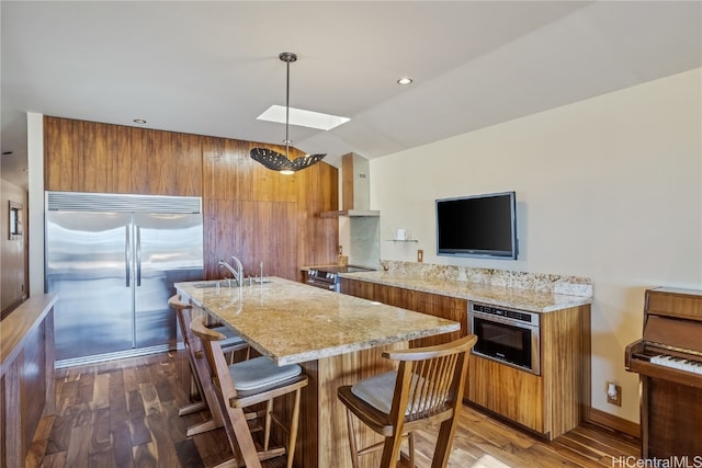 kitchen with appliances with stainless steel finishes, wall chimney range hood, pendant lighting, and dark hardwood / wood-style floors