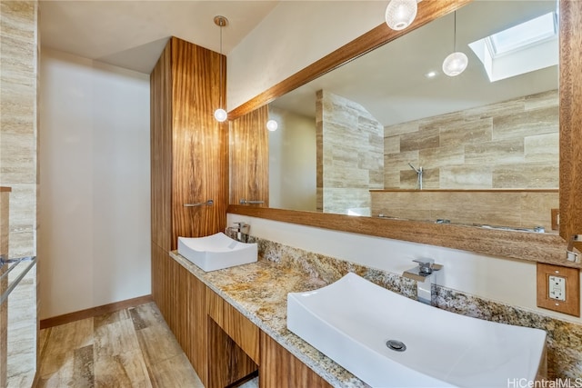 bathroom featuring a skylight, hardwood / wood-style floors, tile walls, vanity, and a shower