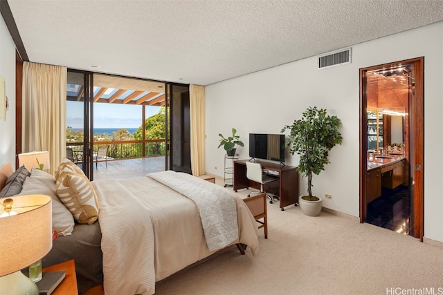 bedroom with a textured ceiling, access to exterior, expansive windows, connected bathroom, and light colored carpet