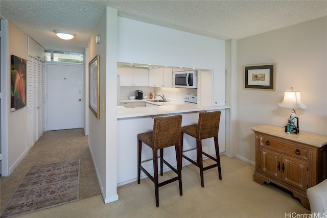 kitchen with a breakfast bar area, sink, light colored carpet, white cabinetry, and a textured ceiling