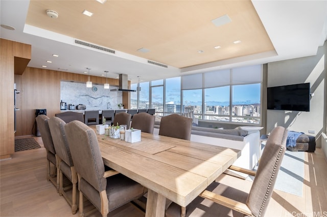 dining space featuring floor to ceiling windows, wood walls, light hardwood / wood-style floors, and a raised ceiling