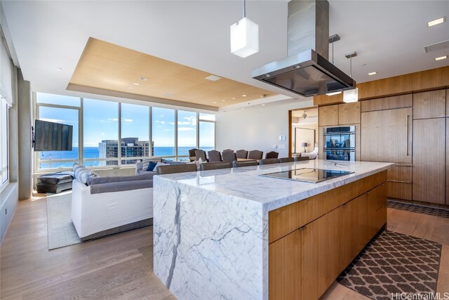 kitchen with a large island, island exhaust hood, stainless steel double oven, and light hardwood / wood-style floors