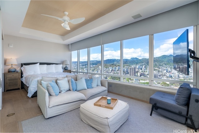 bedroom with hardwood / wood-style floors, a raised ceiling, and ceiling fan