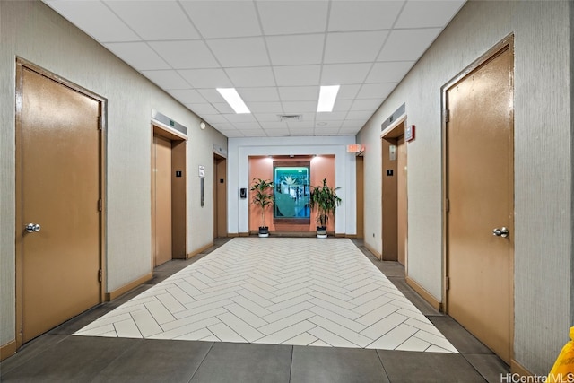 corridor with a paneled ceiling, elevator, and light tile patterned floors