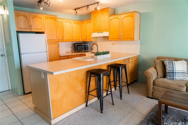 kitchen featuring tasteful backsplash, a textured ceiling, a breakfast bar area, light tile patterned floors, and white refrigerator