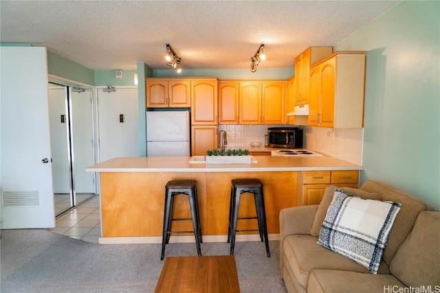 kitchen with light brown cabinets, kitchen peninsula, a breakfast bar area, a textured ceiling, and stainless steel appliances