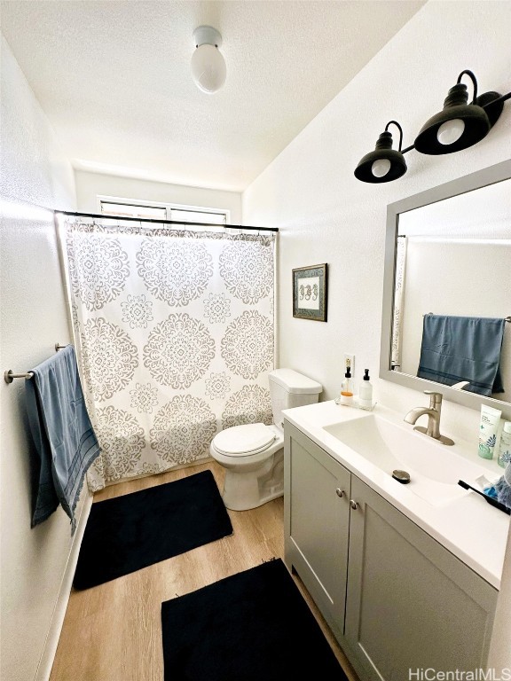 bathroom featuring a textured ceiling, walk in shower, hardwood / wood-style flooring, toilet, and vanity