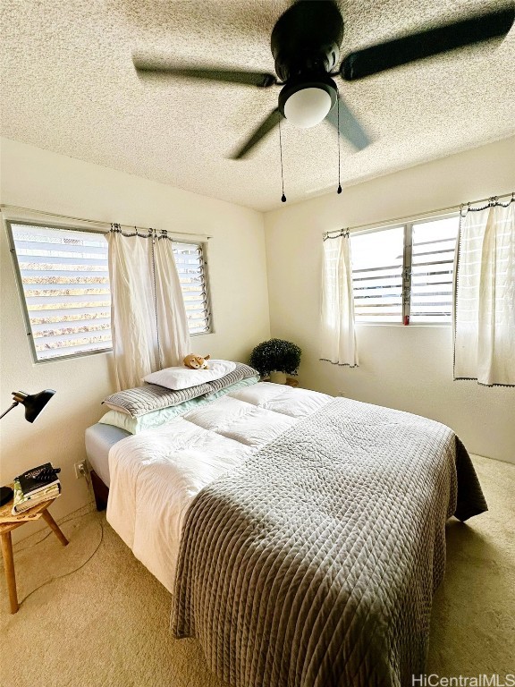 carpeted bedroom featuring a textured ceiling, multiple windows, and ceiling fan